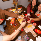 Group of friends enjoying a casual gathering with drinks and snacks on a wooden table.