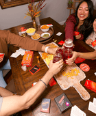 Group of friends enjoying a casual gathering with drinks and snacks on a wooden table.